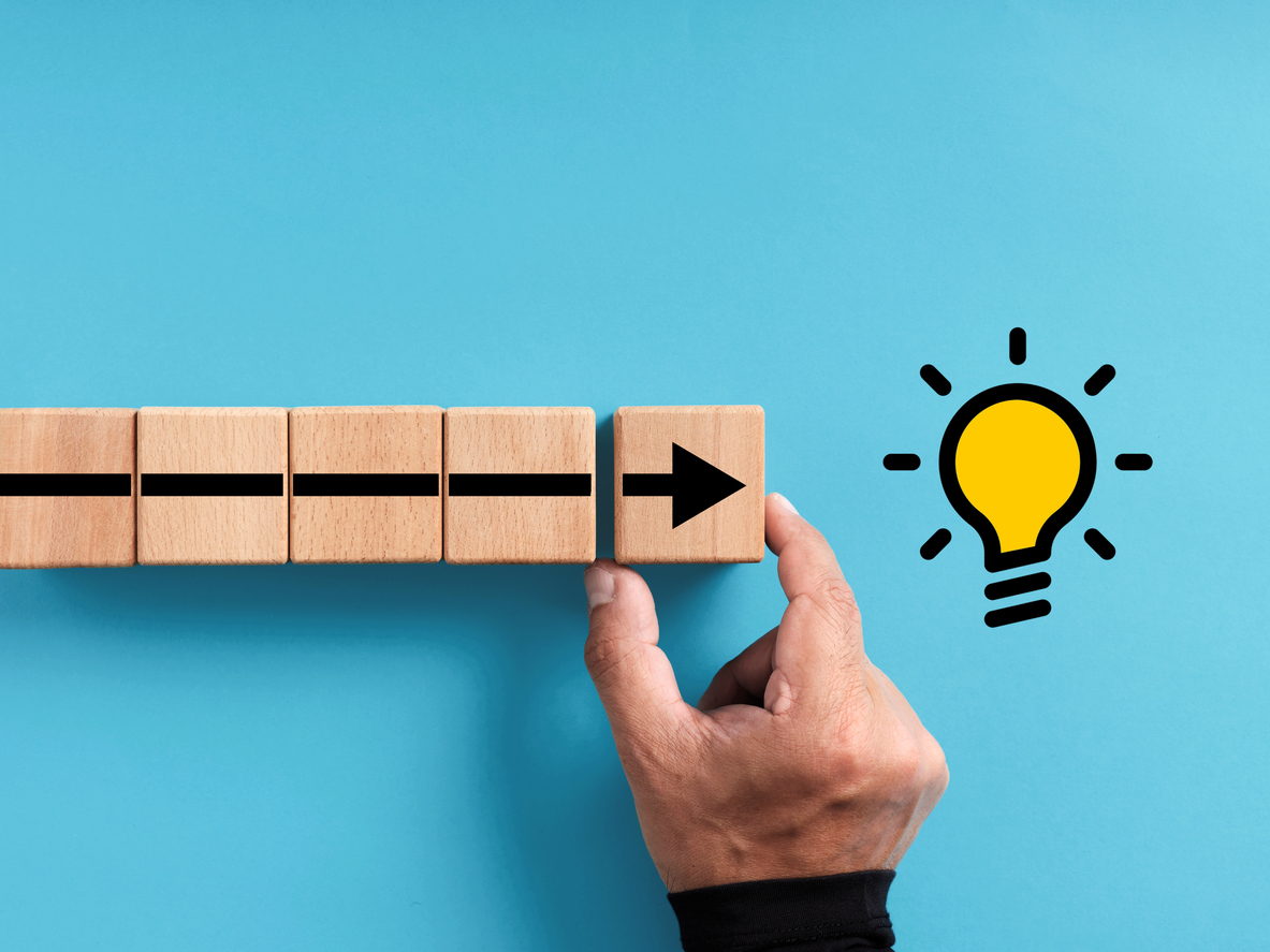 Hand arranges the wooden blocks with the arrow moving towards the light bulb idea icon.