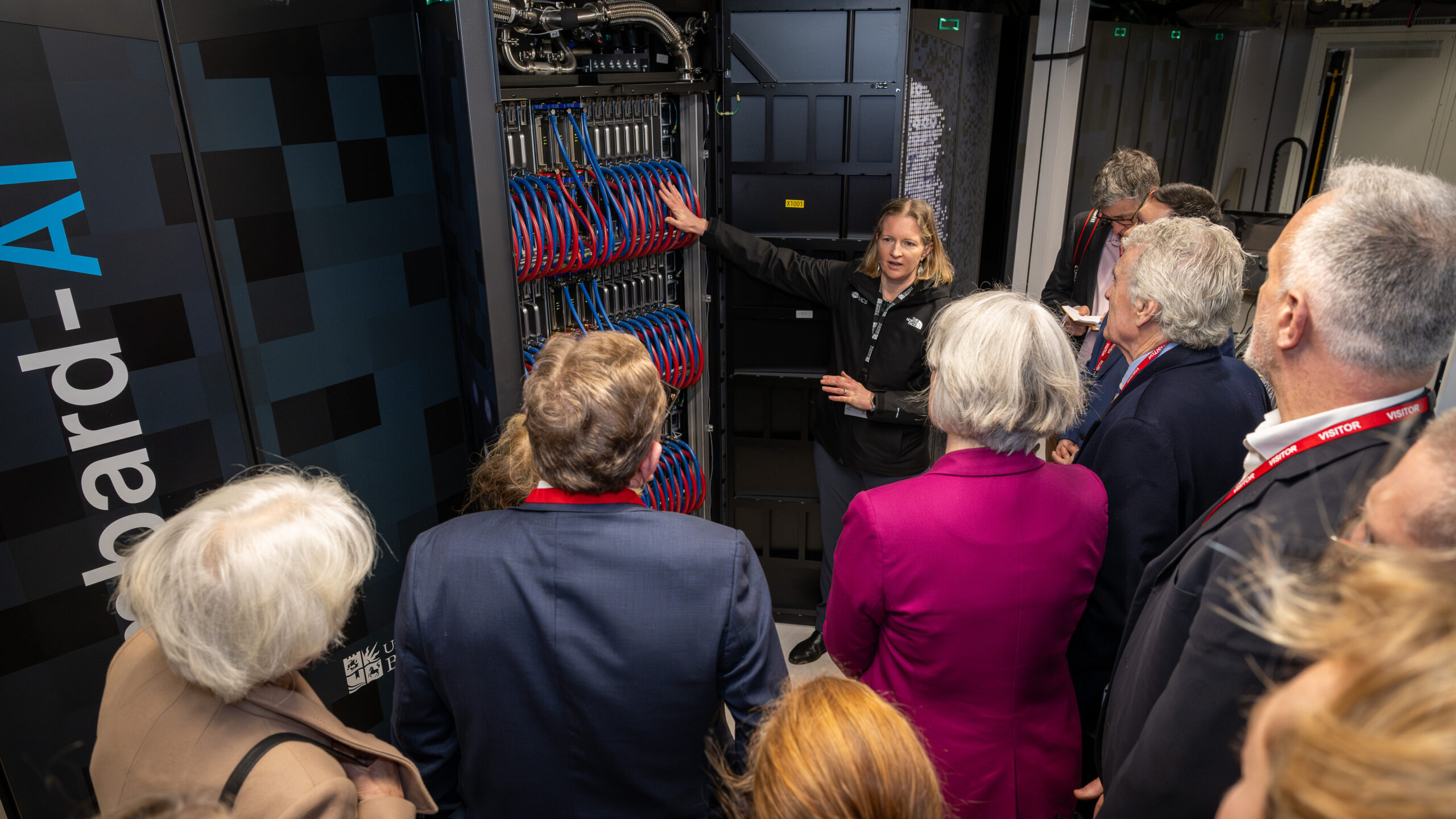 Group of regional leaders on tour of Isambard-AI with tour-guide pointing to part of supercomputer.