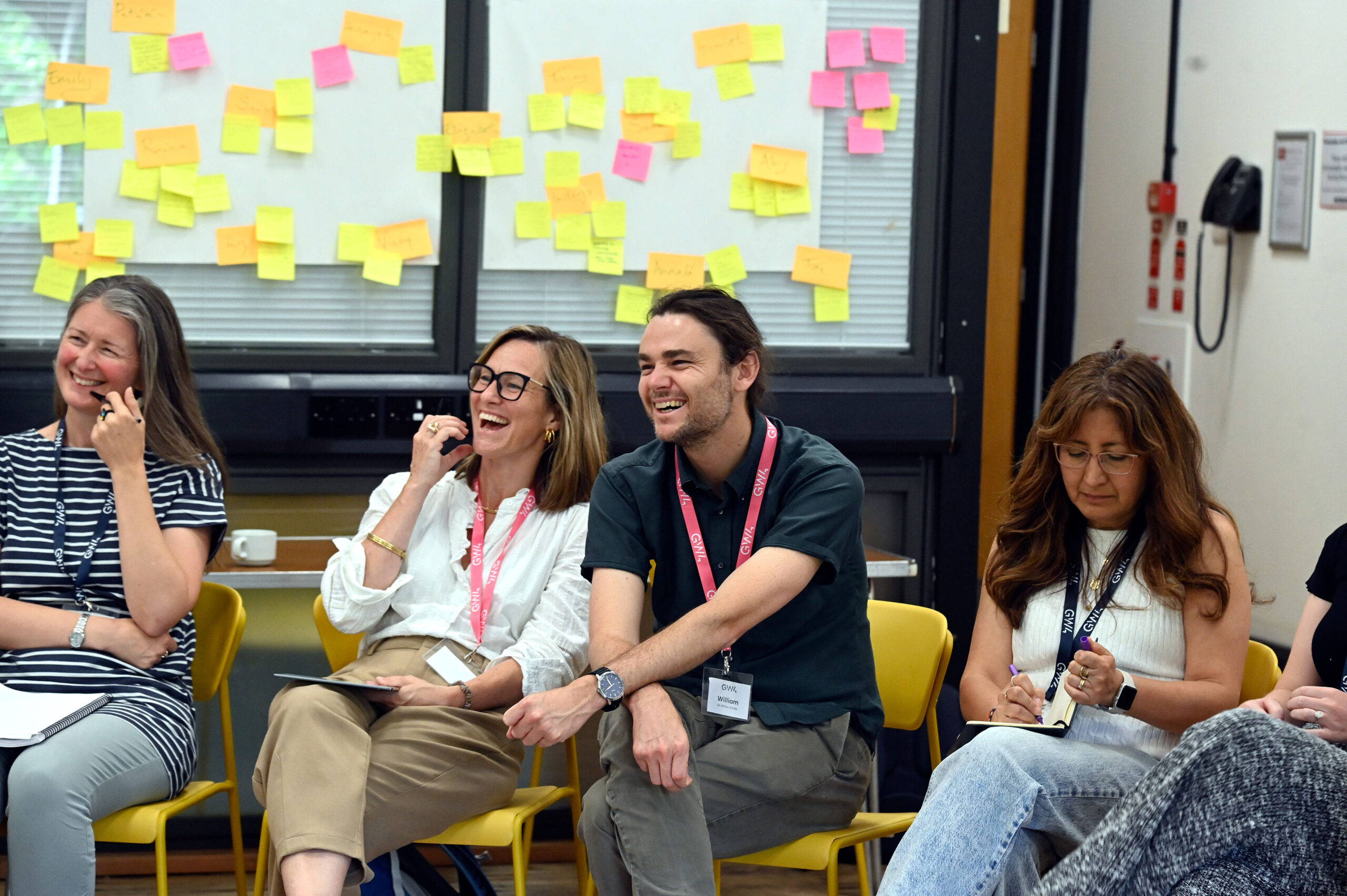 Workshop participants and facilitators sitting and laughing surrounded by post-it notes.